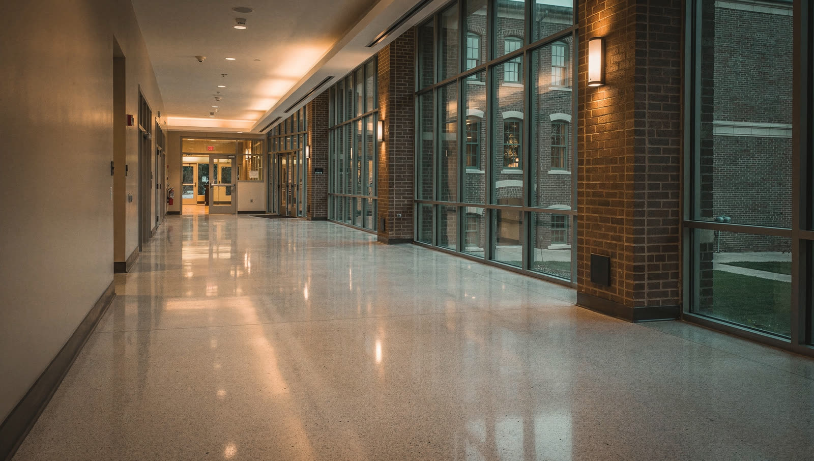 A finished commercial floor in a Central Texas university research building corridor, polished terrazzo-like concrete, brick academic architecture beyond the glass