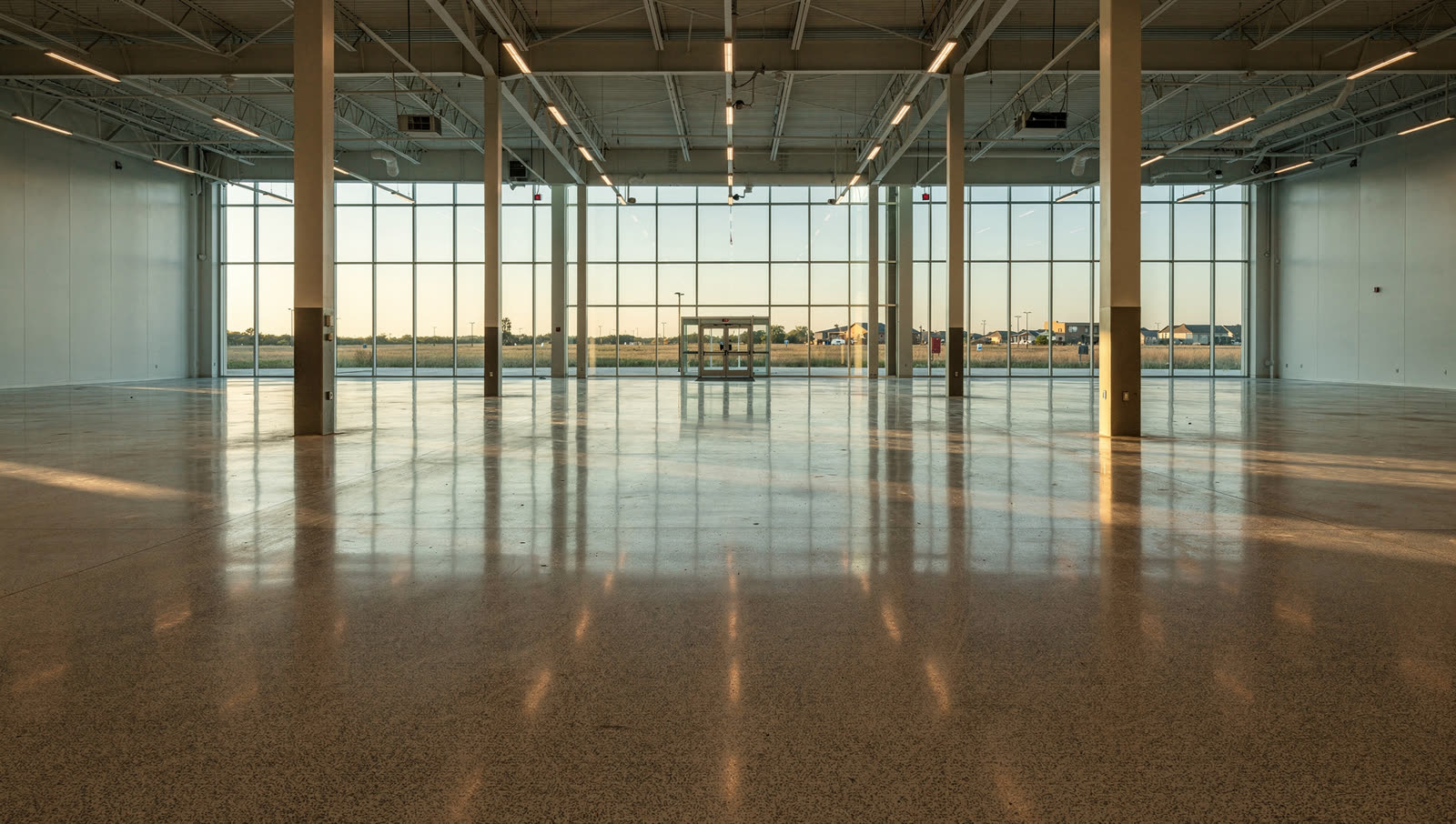 A finished commercial floor in a brand new big-box retail hall in a West Houston master-planned suburb, long clean sightline, flat prairie horizon past the entry glass