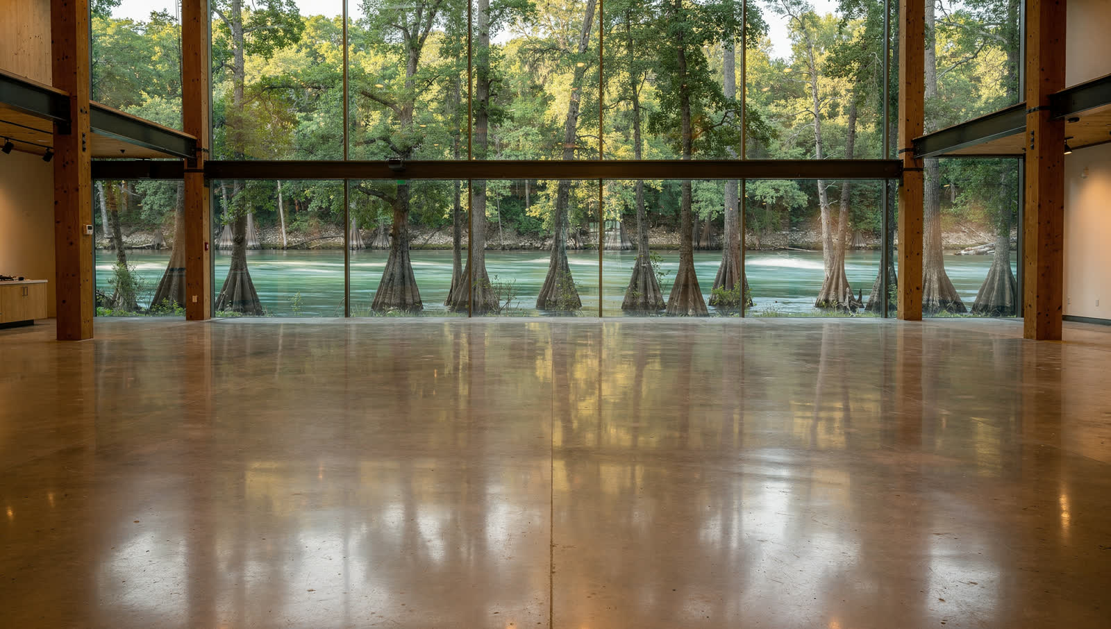 A finished commercial floor in a river town retail hall between Austin and San Antonio, tall glazed front, bald cypress along a clear green river beyond