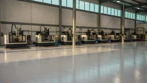 A finished commercial floor in a precision machine shop in a north Dallas trade corridor, machine bases bolted to a sealed floor, clerestory windows