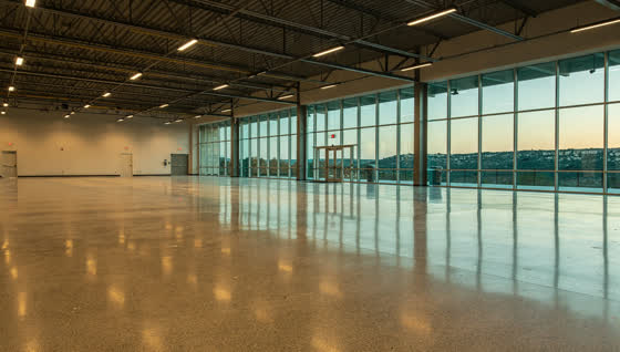 A finished commercial floor in a suburban ice and sports arena concourse northwest of Austin, exposed steel, hill country ridgeline through the glass