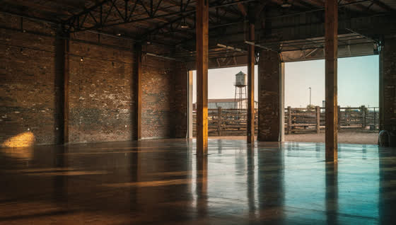 A finished commercial floor in a brick warehouse turned market hall near the historic stockyards, timber posts, cattle pens and water tower beyond