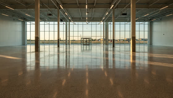 A finished commercial floor in a brand new big-box retail hall in a West Houston master-planned suburb, long clean sightline, flat prairie horizon past the entry glass