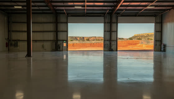 A finished commercial floor in a North Texas industrial workshop on red-bed country, coated floor, red earth and low mesas visible outside